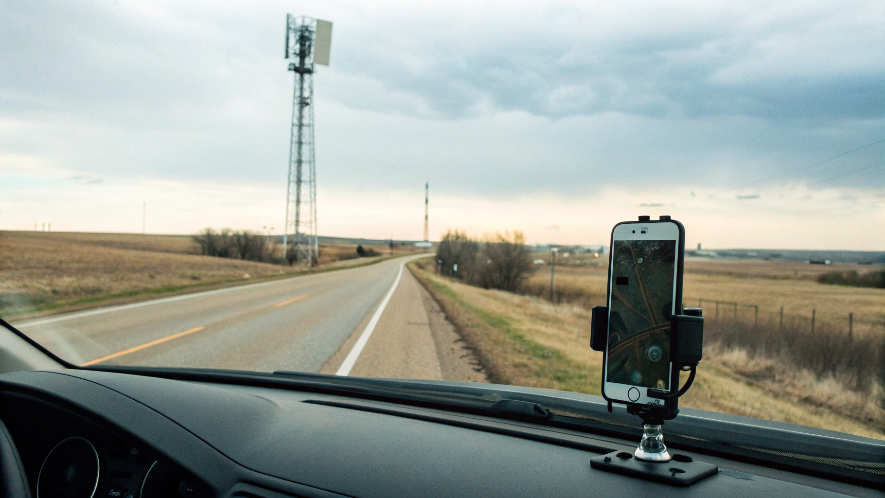 iPhone на держателе в машине, трасса и базовая станция на горизонте