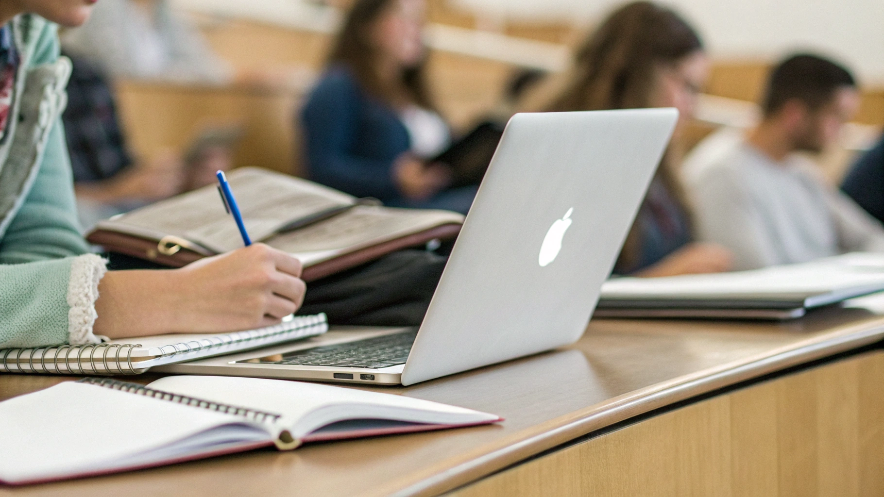MacBook и тетради на парте во время университетской лекции