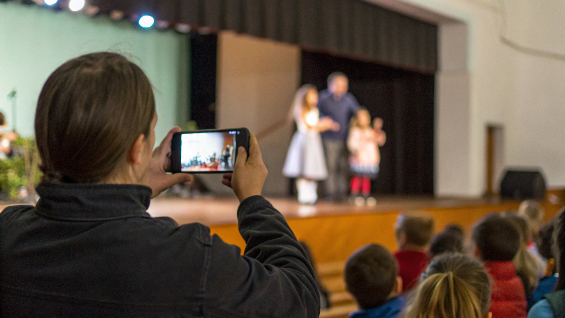 Родитель снимает детский утренник на смартфон из зала