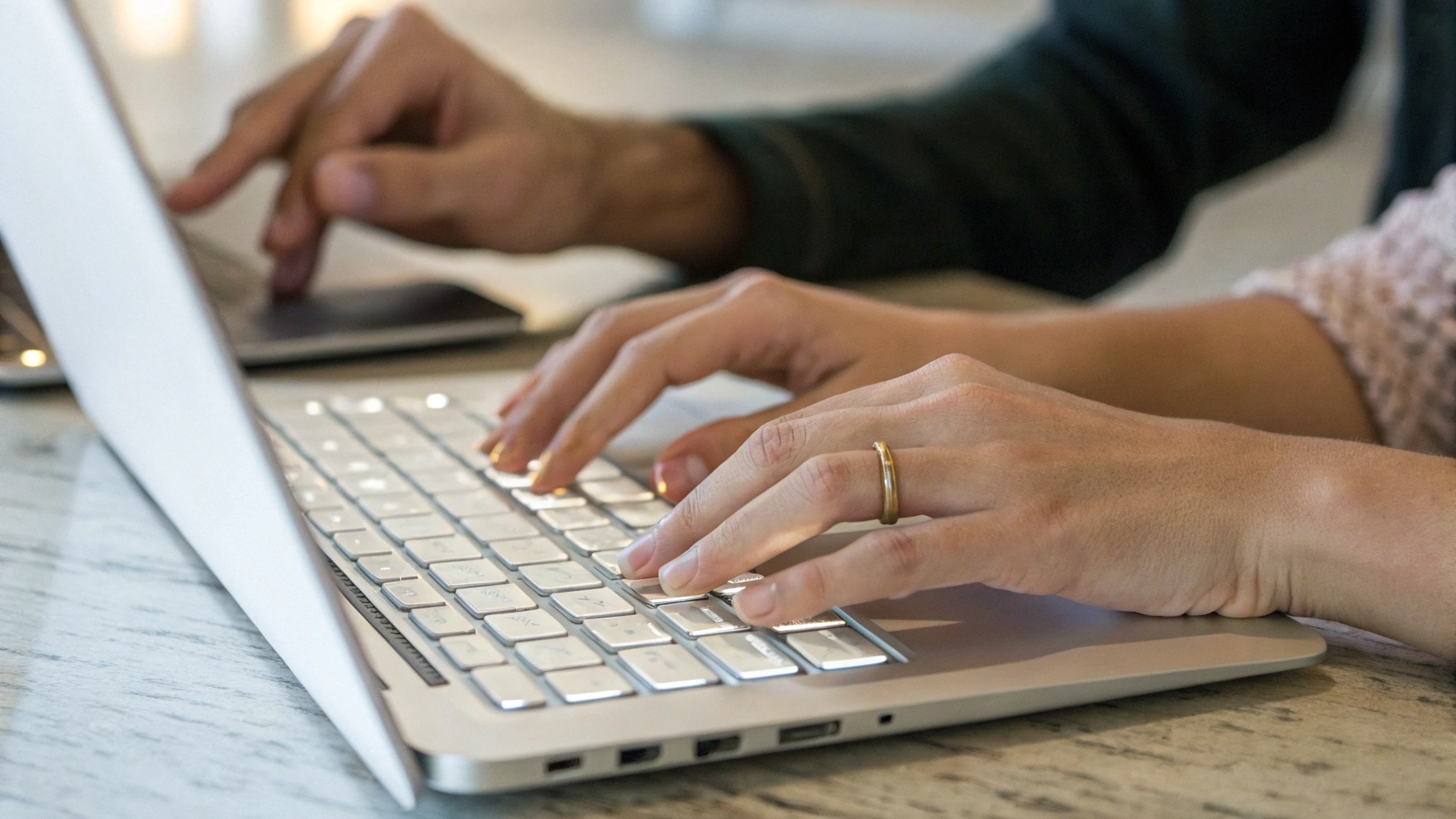 Две пары рук по очереди печатают на клавиатуре одного ноутбука