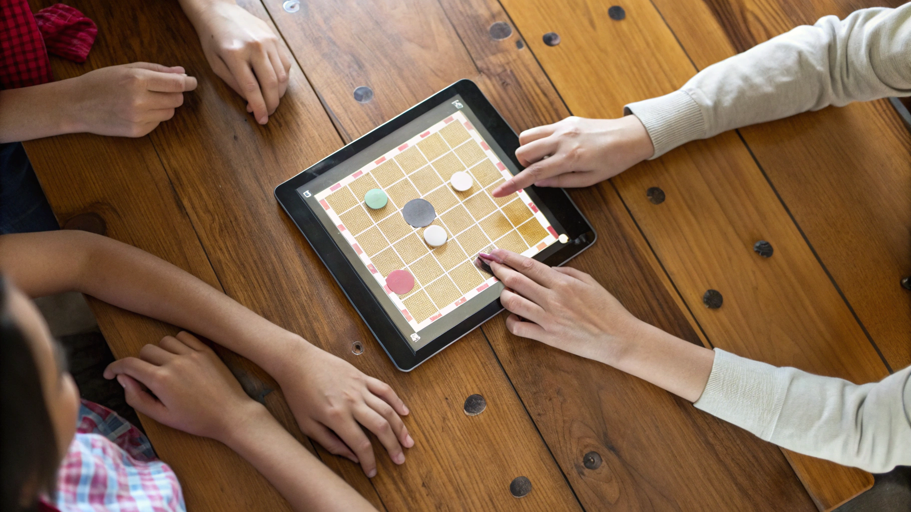Планшет на столе с открытой цифровой настольной игрой и руками игроков вокруг